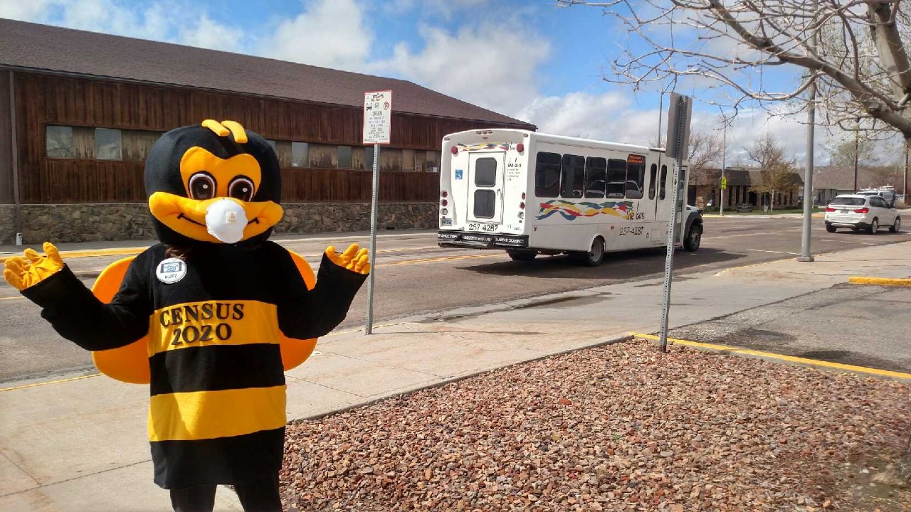 BUZZ the bee stands near a bus a and waves while wearing a mask to slow the spread of COVID-19.